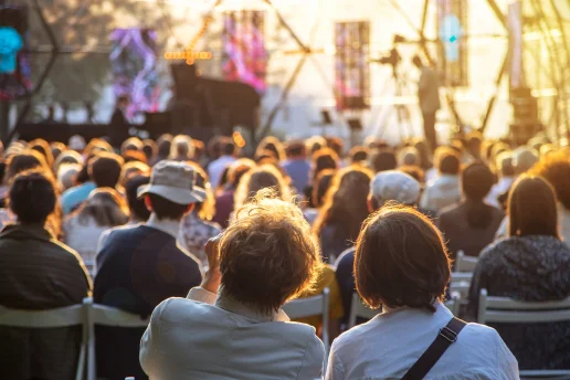 MV-Ostseekooperation Veranstaltung Abendstimmung Blick von hinten auf ein großes Publikum, das in Stuhlreihen ein Open-Air-Konzert besucht. Die Szene ist in das warme Licht der tiefstehenden Abendsonne getaucht, während im Hintergrund eine Bühne mit einem Flügel zu erkennen ist.