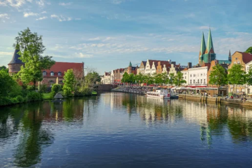 Hansestadt Lübeck – Blick auf Trave, Altstadt und Marienkirche Blick über die Trave auf die Altstadt der Hansestadt Lübeck mit historischen Giebelhäusern, der St.-Marien-Kirche und dem Holstentor im Hintergrund.