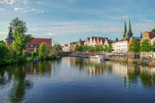Hansestadt Lübeck – Blick auf Trave, Altstadt und Marienkirche Blick über die Trave auf die Altstadt der Hansestadt Lübeck mit historischen Giebelhäusern, der St.-Marien-Kirche und dem Holstentor im Hintergrund.